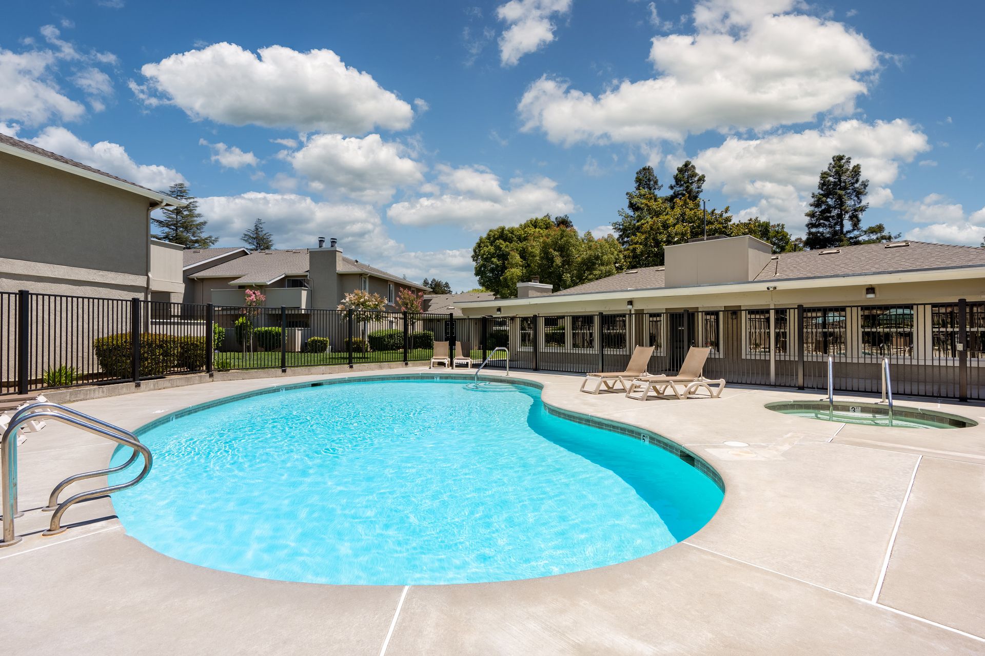 A sparkling blue swimming pool with adjacent spa, loungers and the clubhouse behind it